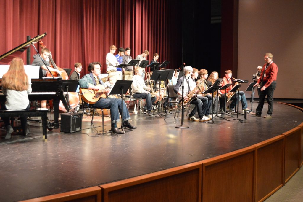 Musicians performing on stage in a school auditorium.