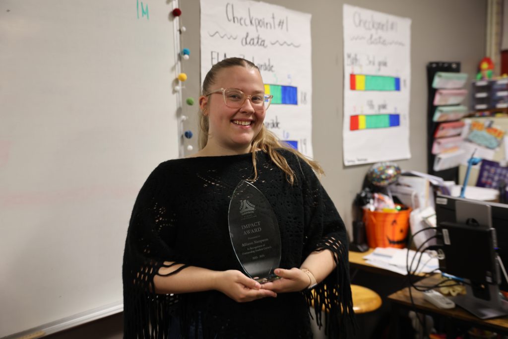 Woman holding a trophy in front of a classroom setting.