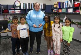 Woman standing in front of children, posing for a picture. They are all smiling and seem to be enjoying themselves.